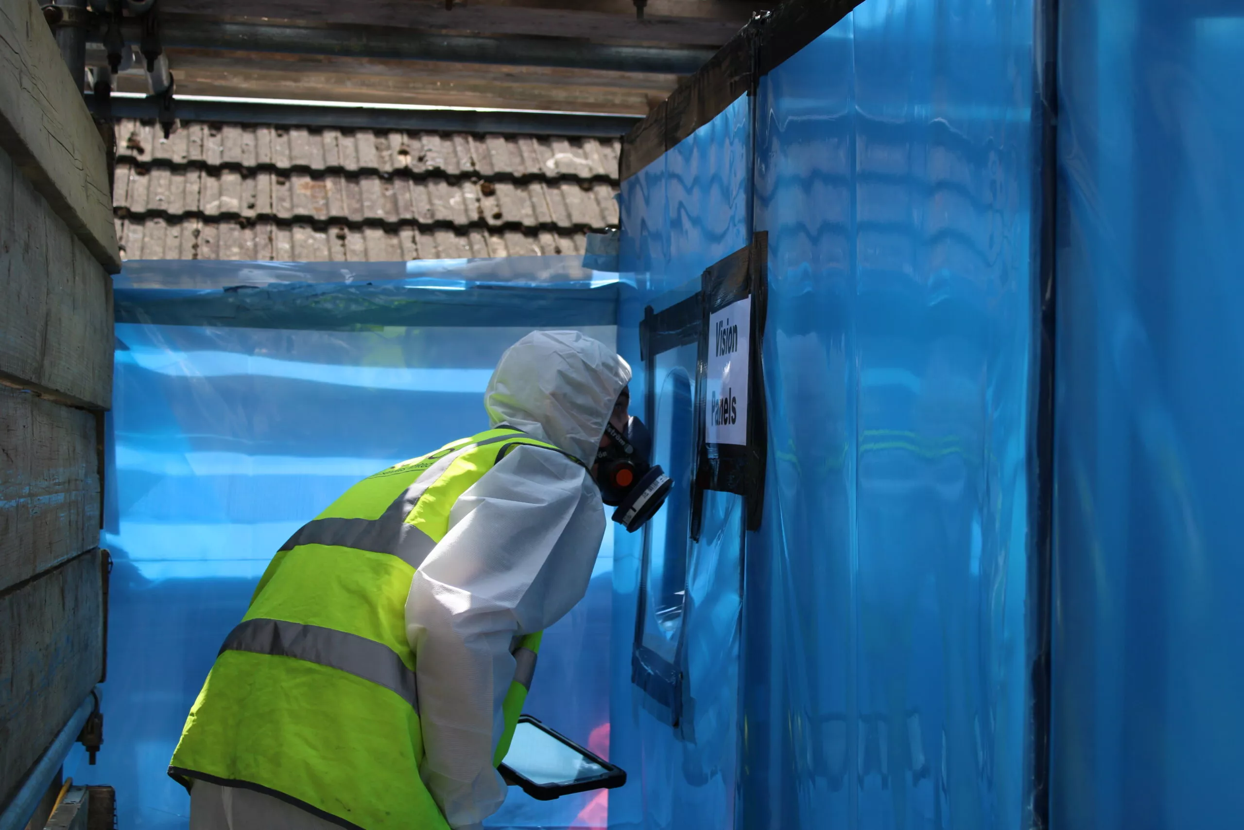 Licensed asbestos removal operatives working inside a sealed enclosure with negative pressure units